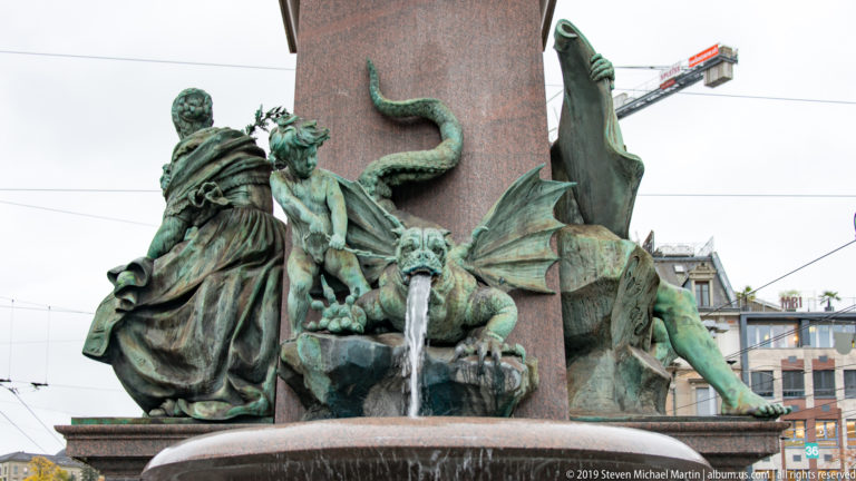 Patinated bronze figures and animal forms around the fountain base of the Alfred Escher monument at Bahnhofplatz in Zurich.