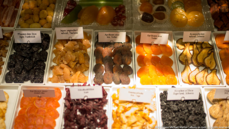 Compartmented display of assorted dried and candied fruits in dark, orange, yellow, and pale tones.
