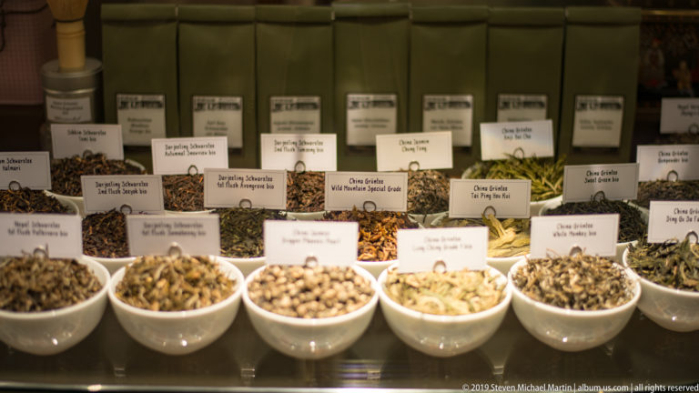 Rows of white bowls containing different loose-leaf teas, each identified by a small printed label.
