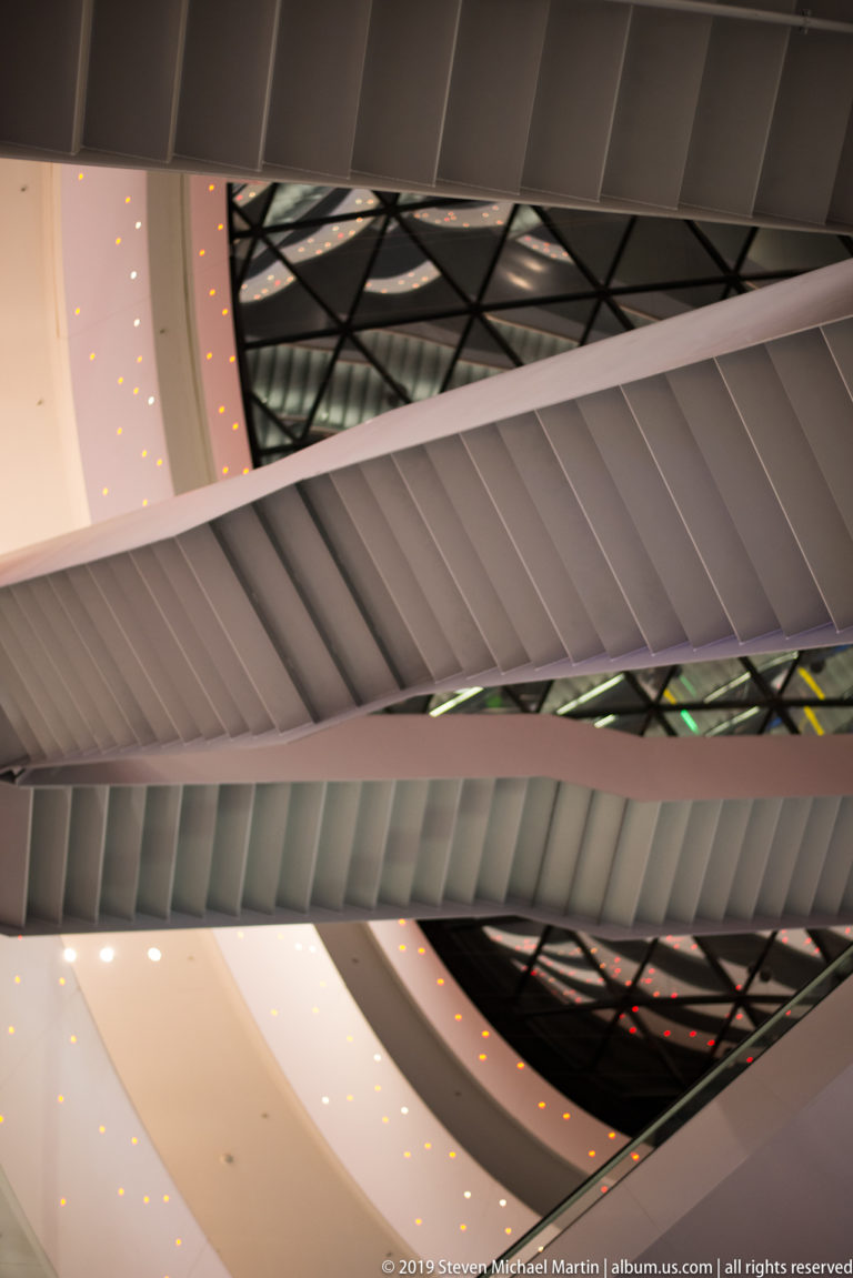 White curved ceiling bands intersect beneath a dark glazed roof structure, with small recessed lights visible along the surfaces.