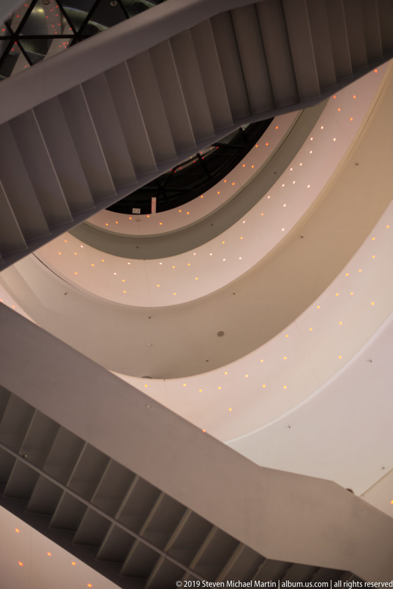 Curving white ceiling planes with tiny warm lights beneath dark structural ribs in a modern Zurich interior.