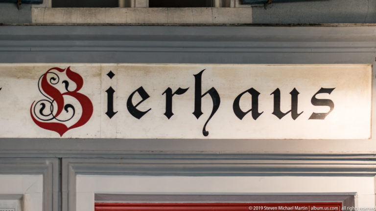 Illuminated sign reading “Bierhaus” in black decorative lettering with an ornate red initial.