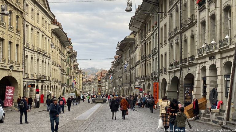 Busy pedestrian street in Bern’s Old City lined with arcaded historic façades and shops.