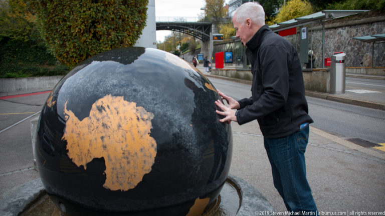 Man touching a large black public globe sculpture beside a street in Bern.