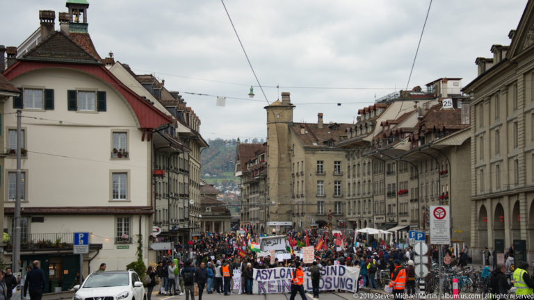 Large street demonstration with banners and flags occupying a historic street in Bern.