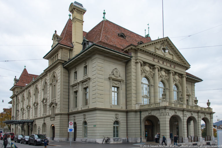 Large historic stone civic building with arched loggia, pilasters, and red-tiled roof in Bern.
