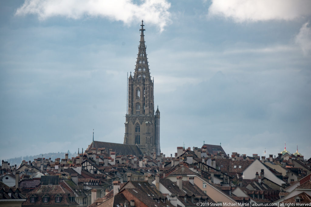 Gothic tower of Bern Minster rising above densely packed red-tiled rooftops.