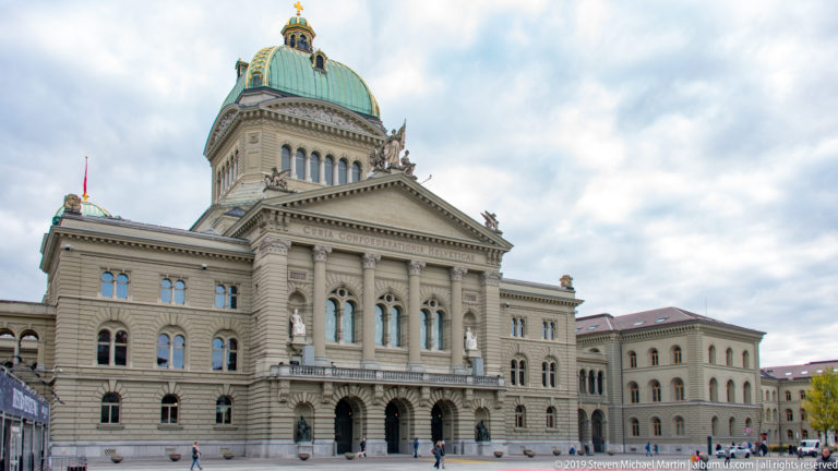 Front view of the Swiss Federal Palace in Bern with green dome, central pediment, and symmetrical wings.