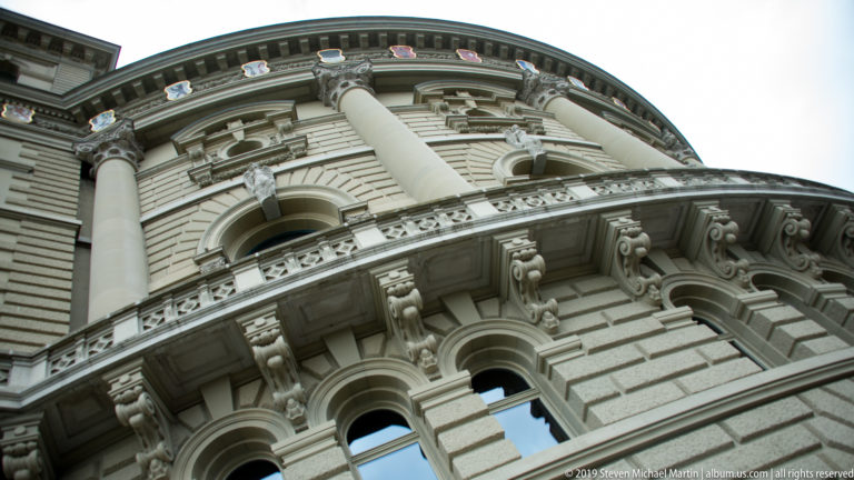 Low-angle view up the Swiss Federal Palace façade with rusticated stonework, arched windows, and columns.