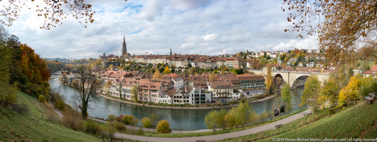 Wide autumn panorama of Bern’s Old City inside the Aare bend with a large stone bridge at right.