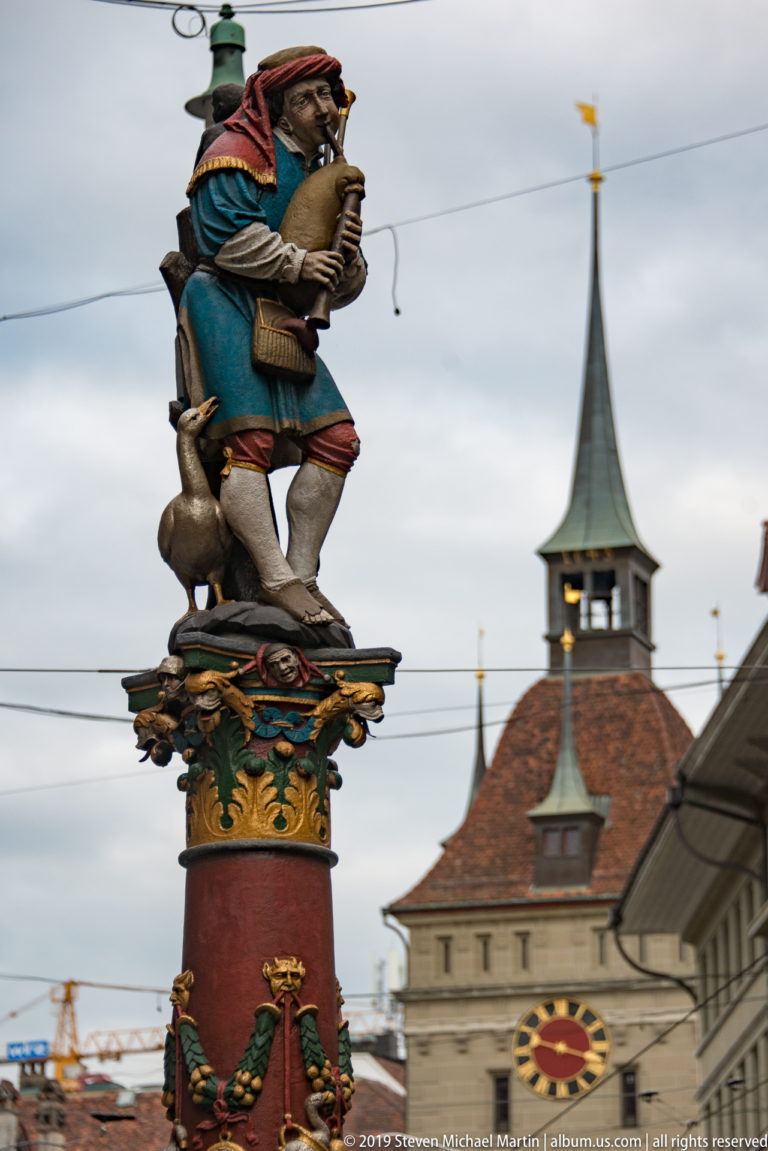 Colorful bagpiper fountain figure with a small animal atop a red column in Bern.