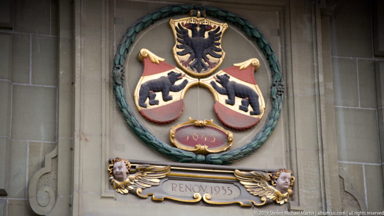 Polychromed heraldic relief with black eagle, two black bears, green wreath, and a restoration inscription.