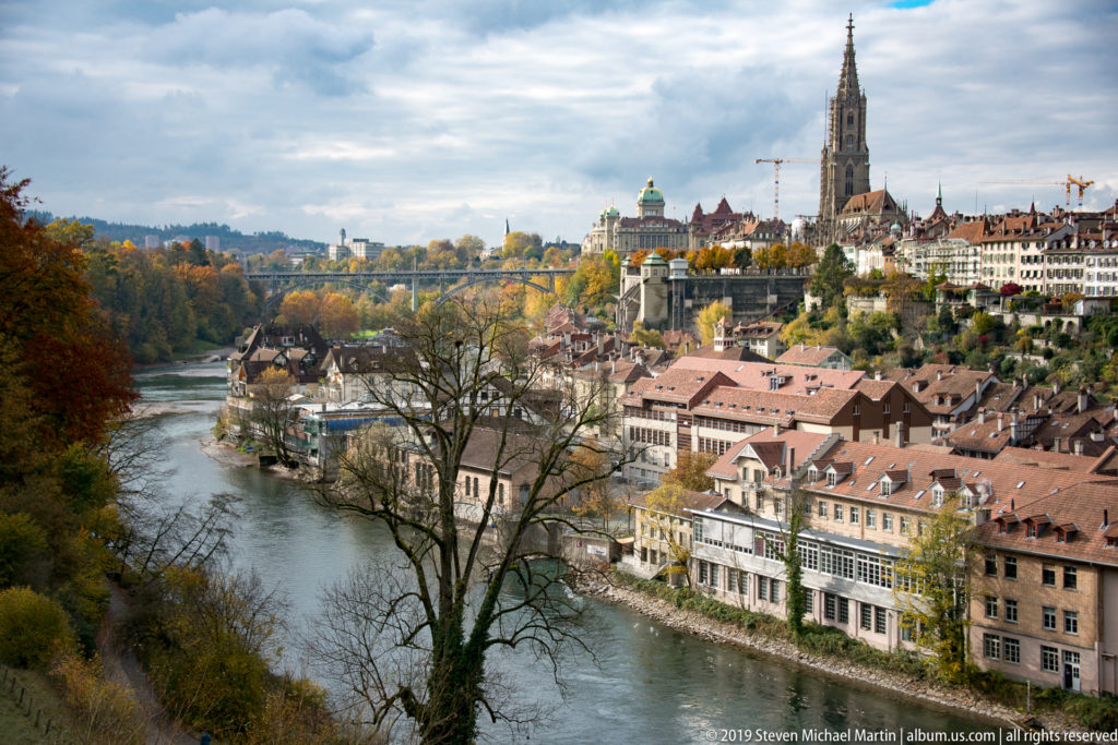 Aare River beside historic buildings with Bern Minster tower rising on the ridge beyond.