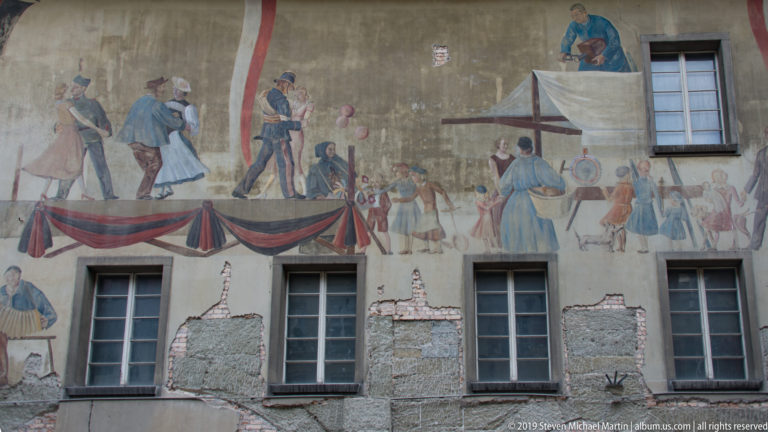Weathered historic mural with a procession of figures in period dress across a Bern façade.