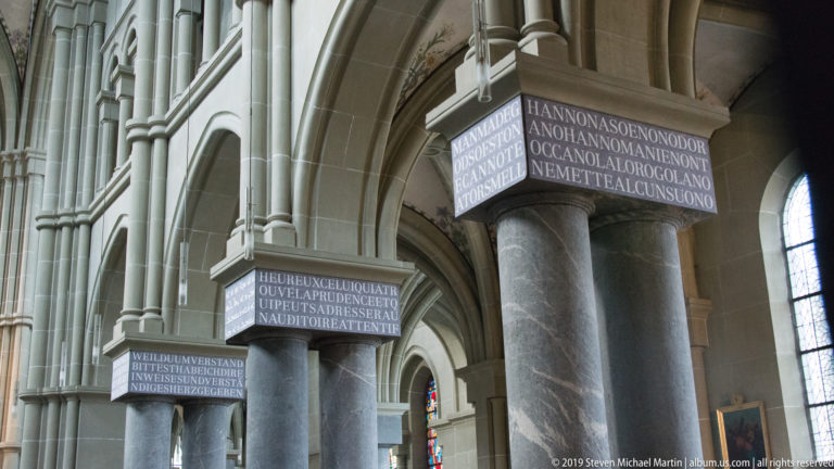 Clustered stone columns inside Bern Minster with broad inscribed bands around their capitals.