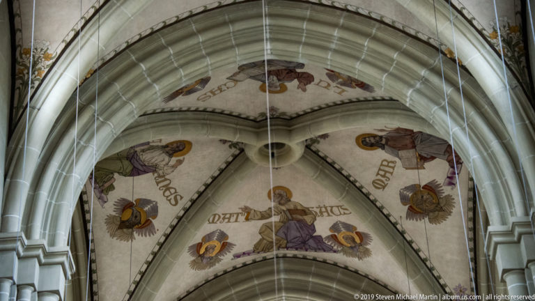 Ribbed vault in Bern Minster decorated with painted figures and large inscriptions.