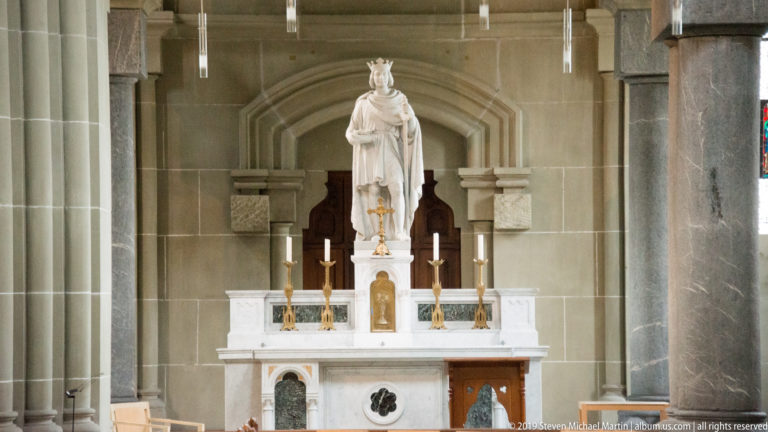 White side altar with candles, gilded objects, and a crowned female statue in Bern Minster.