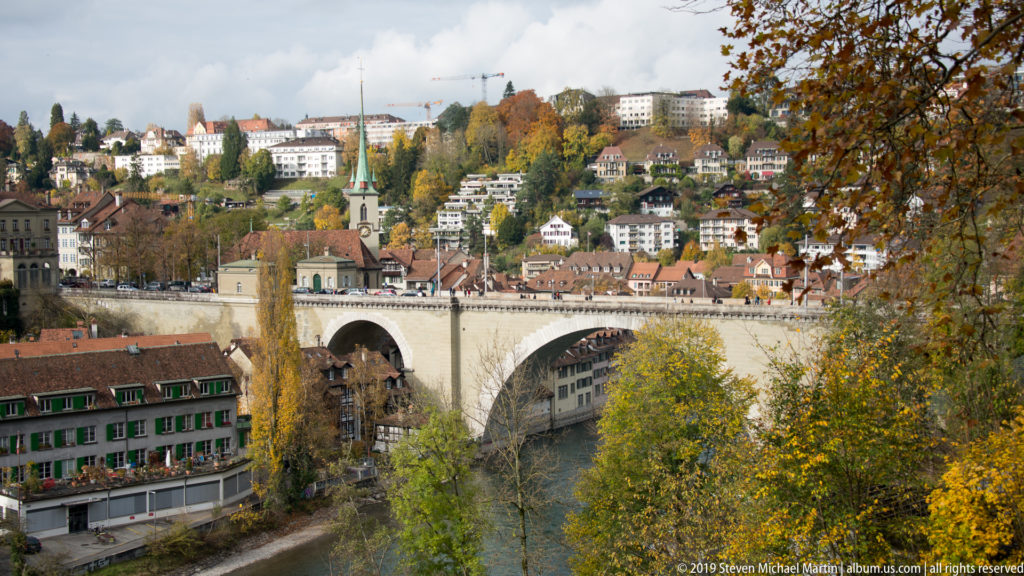 Large stone arch bridge crossing the Aare with a green church spire and hillside houses beyond.