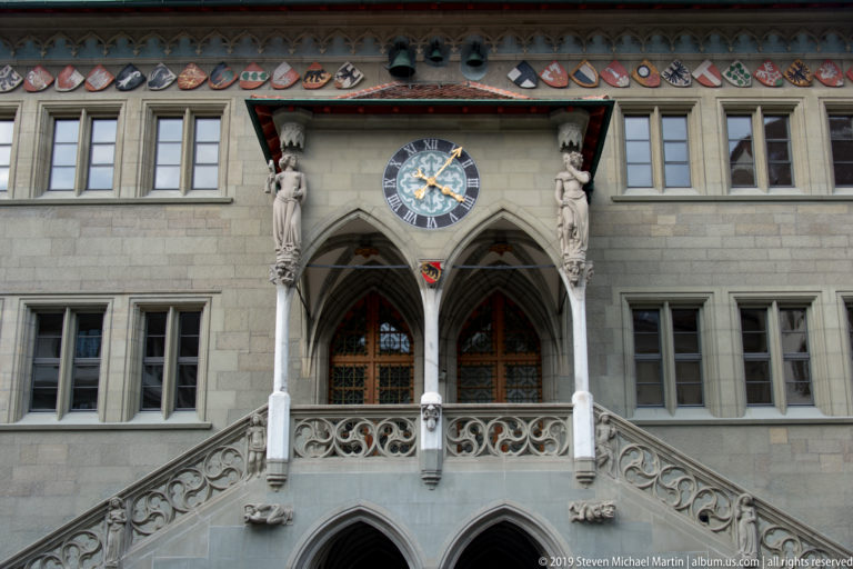 Closer view of Bern Town Hall’s central loggia, clock, sculpted figures, heraldic shields, and twin stairs.
