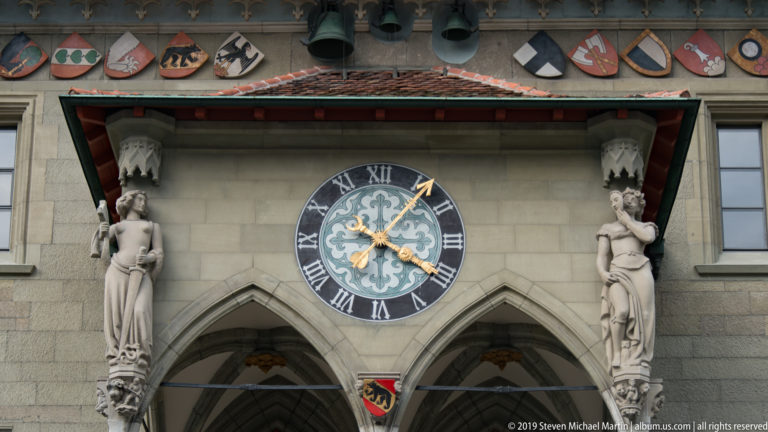 Decorative blue-and-gold clock flanked by stone figures above the Gothic arches of Bern Town Hall.