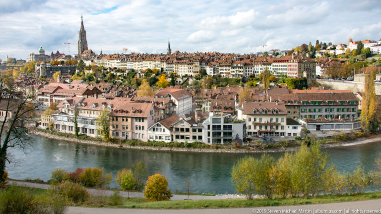 Historic Bern buildings lining a curve of the Aare beneath a densely built hillside.