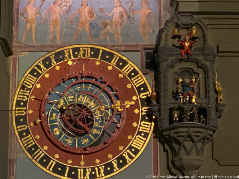 Close night view of the Zytglogge astronomical dial with zodiac rings and adjacent mechanical figures.