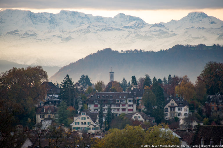 Autumn hillside neighborhood in Bern with mist and snow-covered Bernese Alps rising across the background.
