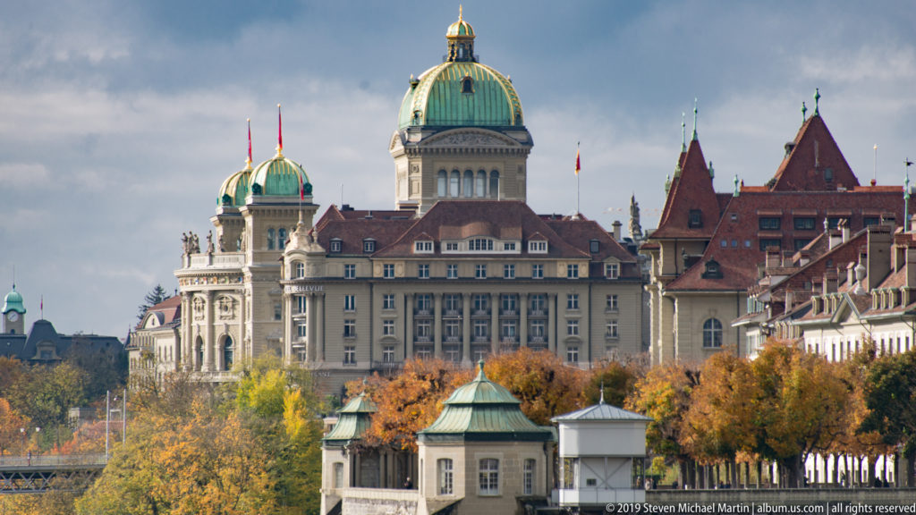 Green Federal Palace dome above civic buildings, red roofs and autumn trees in Bern.