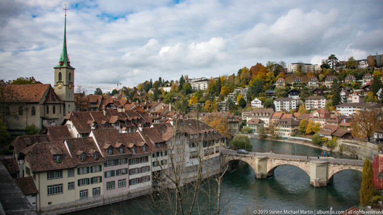 Historic stone bridge crossing the Aare below Bern rooftops and a green-spired church.