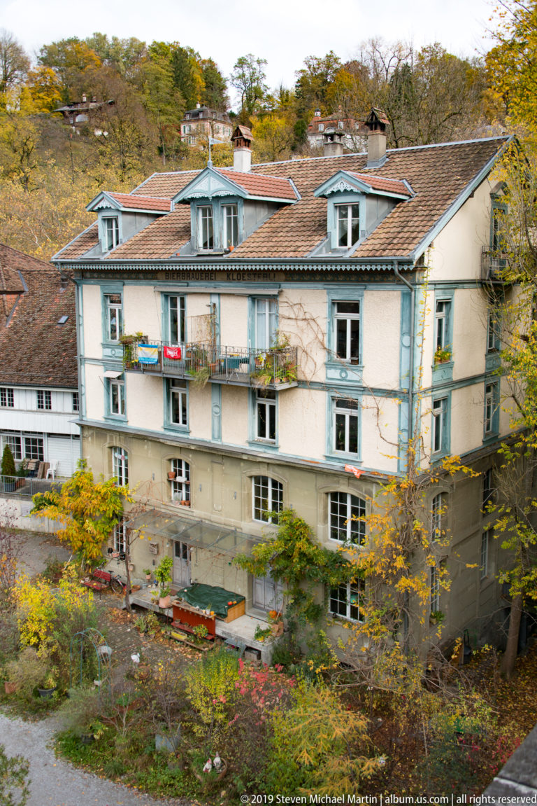 Pale multi-story Bern residence with blue-gray trim, dormer windows, balconies and a garden.