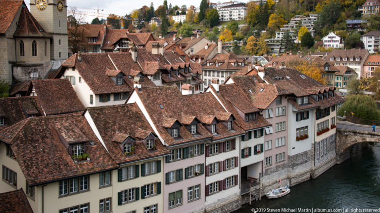 Tightly packed historic houses with red-tiled roofs lining the Aare River in Bern.
