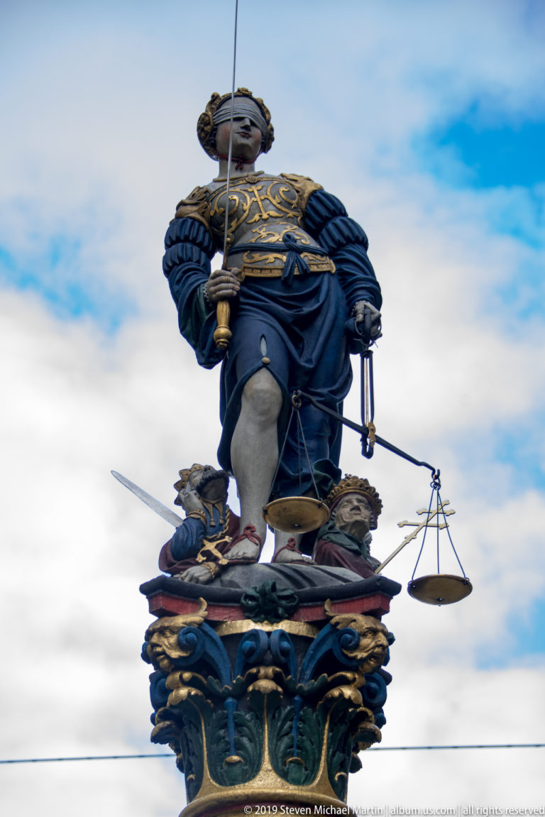 Blindfolded crowned Justice figure holding a sword and scales atop a richly painted Bern fountain.