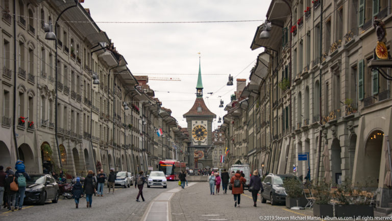 Busy Bern Old Town street lined with arcaded buildings, looking toward the Zytglogge clock tower in the distance.