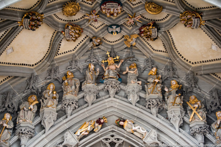 Ribbed Gothic vault above Bern Minster’s west portal with painted bosses, heraldic emblems, and sculpted ornament.