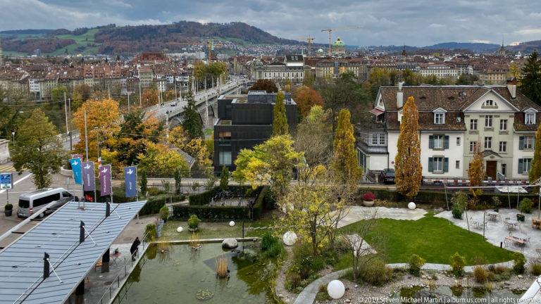Elevated view over a landscaped garden toward Bern buildings and low hills in autumn.