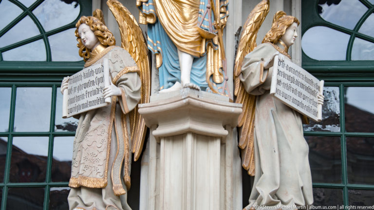 Two gilded-wing angels holding inscribed panels beside the Bern Minster west portal.