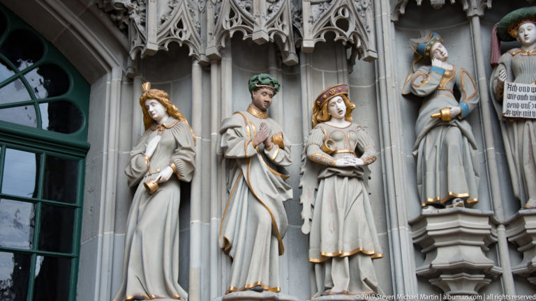Four standing polychromed figures in Gothic niches along the Bern Minster west portal.