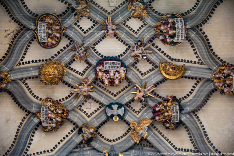 Decorated ribbed vault with painted bosses, coats of arms, and small figures above Bern Minster’s portal.