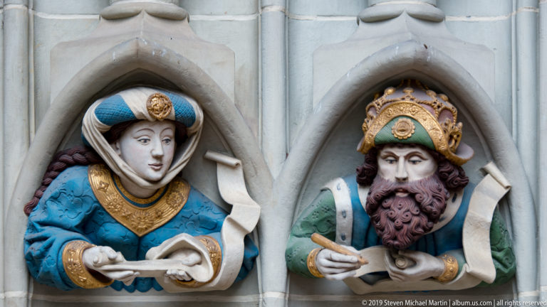 Two polychromed bust figures in pointed niches, one holding a scroll and one writing on a document.