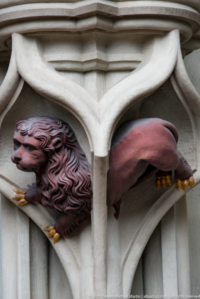 Polychromed winged lion-like grotesque projecting from a carved stone compartment at Bern Minster.