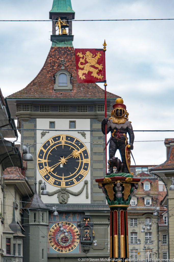 Closer view of the Zytglogge clock faces with the armored-bear Zähringerbrunnen fountain in front.