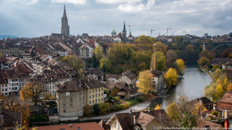 Bern rooftops and Minster tower overlooking a curve of the Aare River in autumn.