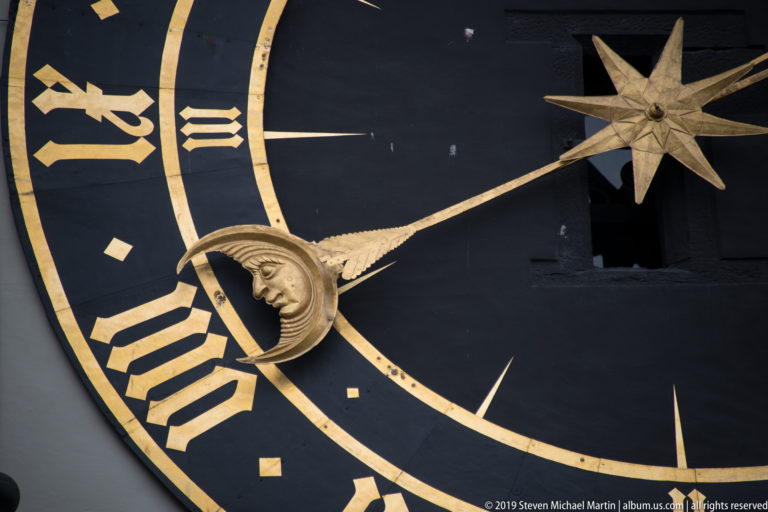 Close view of crescent moon and star pointers crossing the black-and-gold Zytglogge clock face.