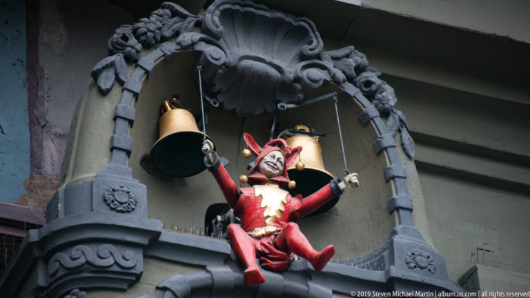 Red jester automaton hanging beneath two bells in the Zytglogge clock mechanism.