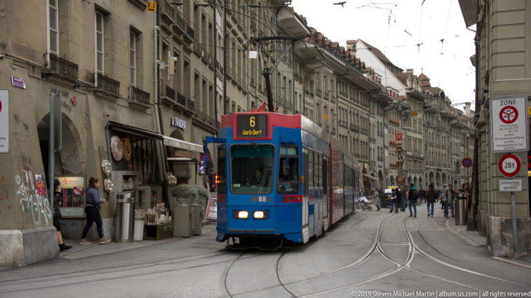 Blue-and-red route 6 tram traveling through a narrow historic street in central Bern.