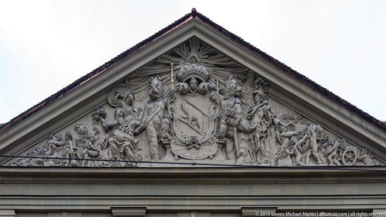 Triangular stone pediment filled with allegorical figures around a central coat of arms.