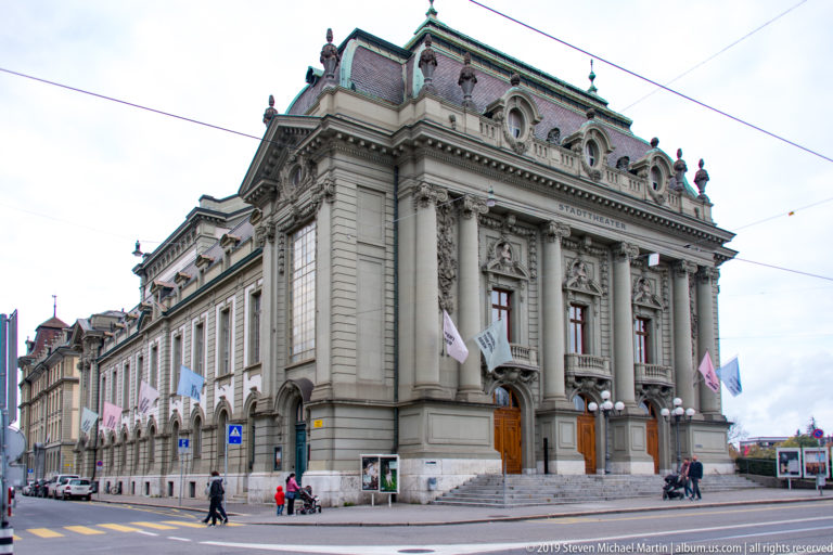 Corner view of the Stadttheater Bern with monumental stone façade, arched windows, and flags.