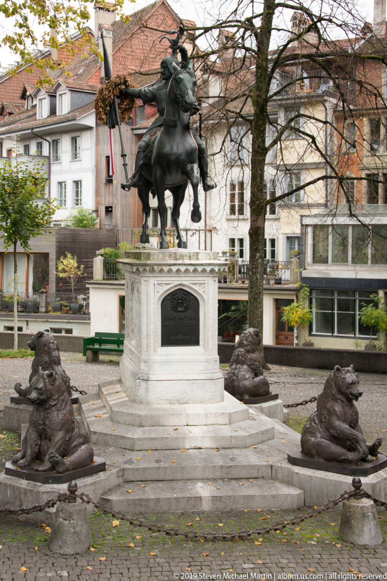 Bronze equestrian monument on a white pedestal surrounded by four recumbent animal sculptures.