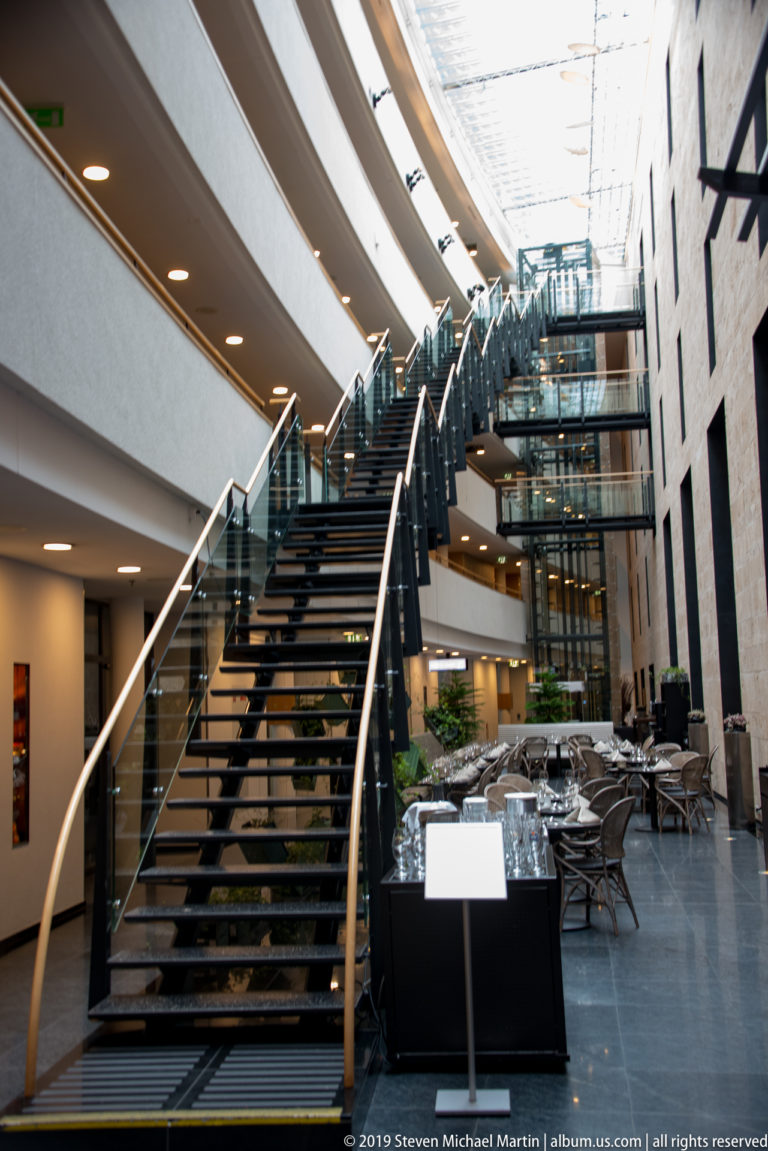 Curving staircase with glass railings rising through a bright multi-level modern atrium.