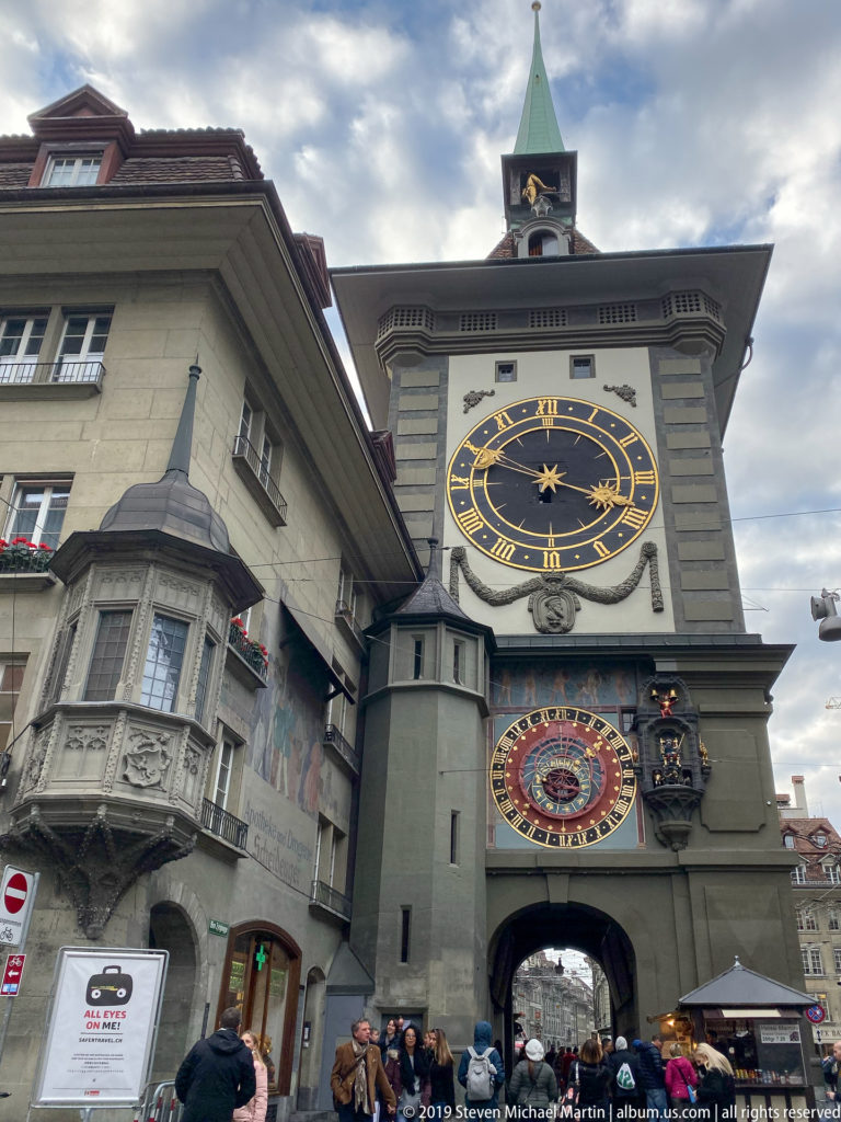 Street-level view of Bern’s Zytglogge showing upper clock, astronomical dial, archway, and neighboring buildings.